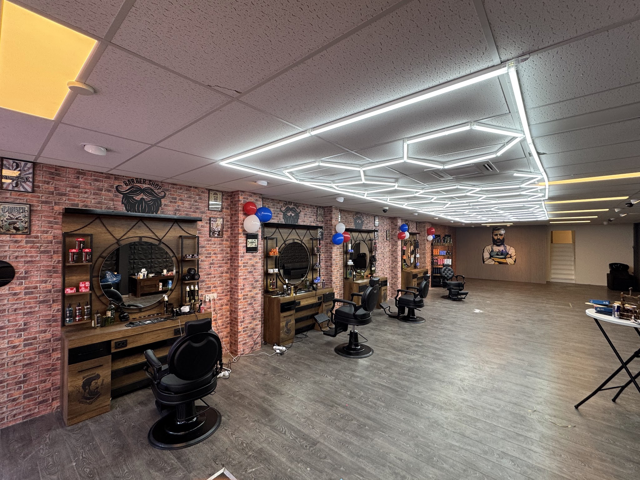 Interieur van Barbershop Miro2: houten werkplekken met ronde spiegels tegen een bakstenen muur, zwarte barbierstoelen en een plafond met zeshoekige ledlampen